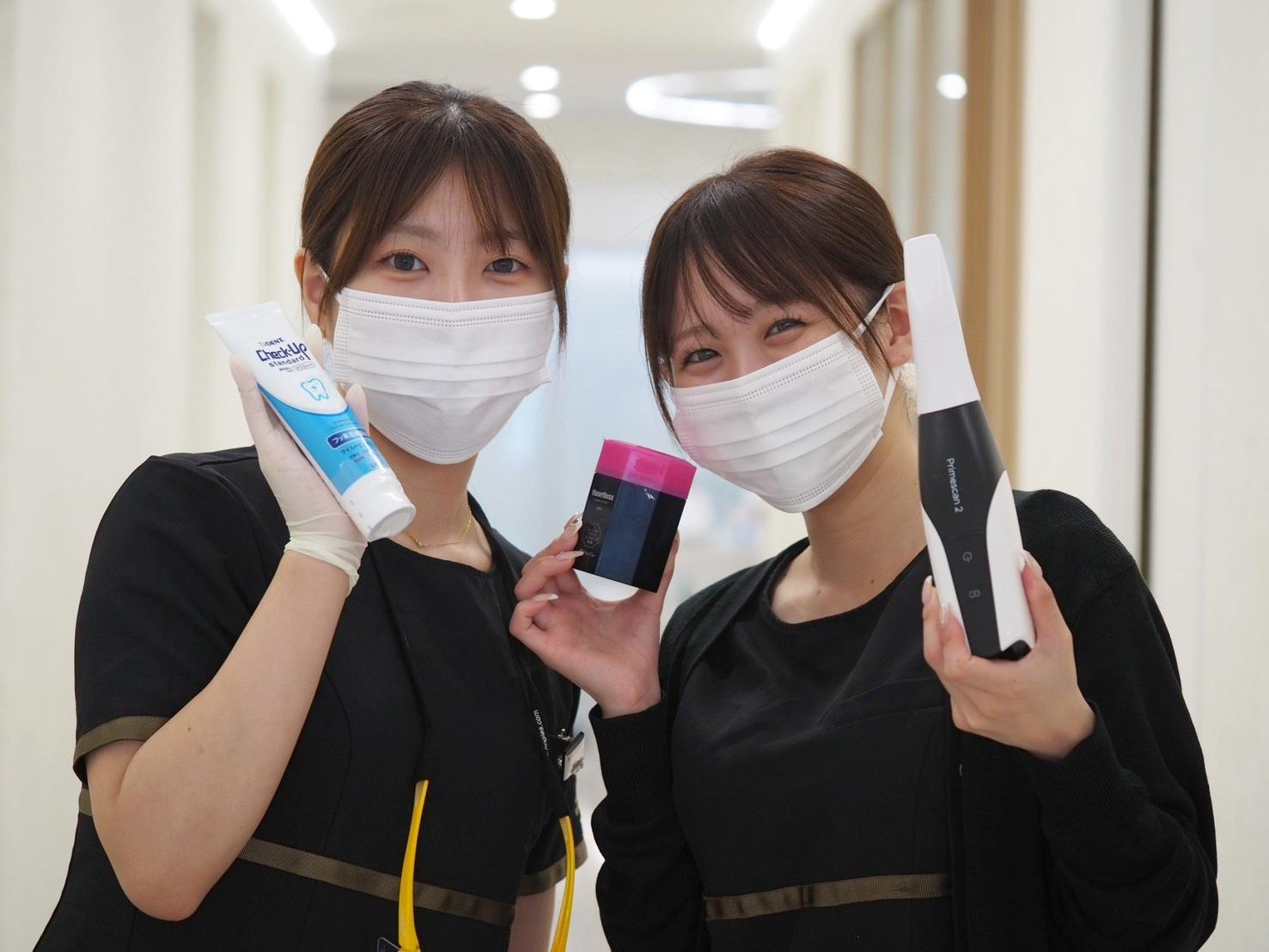 歯科衛生士のスタッフ2名が歯科用品を手に笑顔で並ぶ様子
